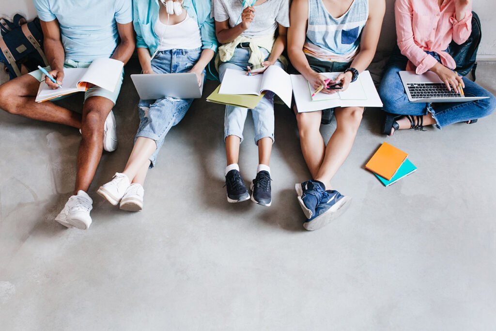 portrait de jeunes gens avec des ordinateurs portables et des smartphones assis ensemble sur le sol les etudiants ecrivant des conferences tenant des manuels sur leurs genoux